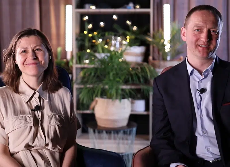 Małżeństwo siedzące na fotelach i patrzące w obiektyw aparatu.