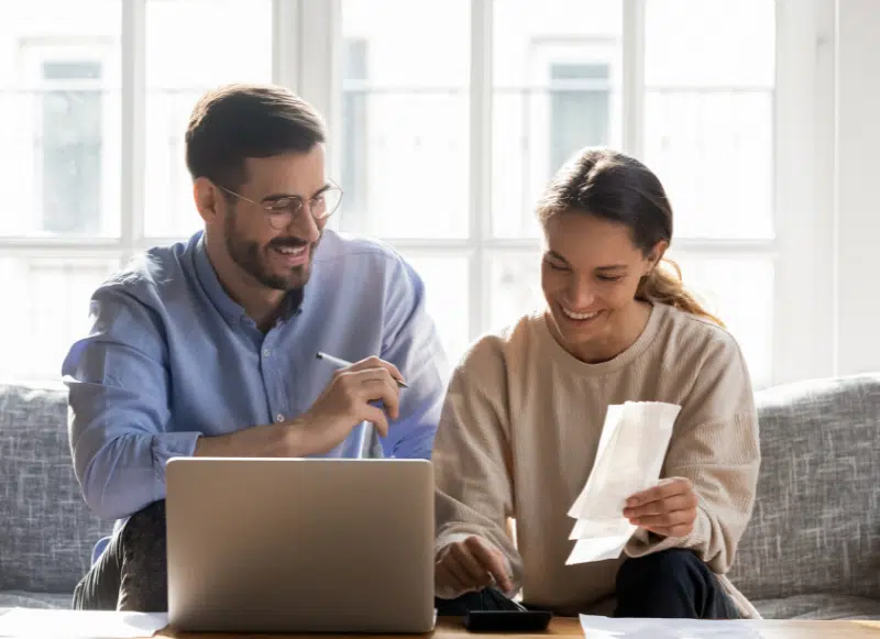Uśmiechnięta para siedząca na kanapie i przeglądająca rachunki i paragony.