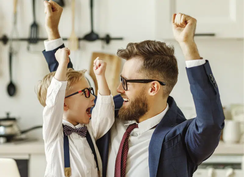 ojciec trzyma dziecko na kolanach i podnoszą ręce ku górze