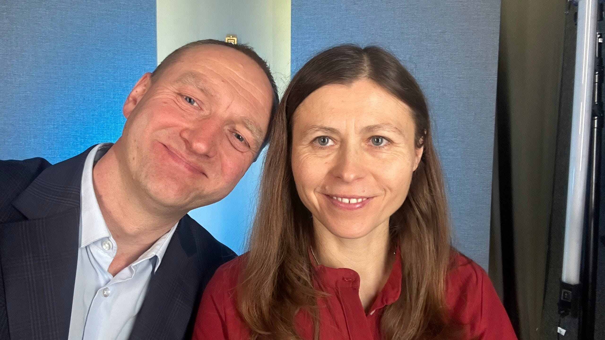 Nie znam osób na zdjęciu, ale widać dwie uśmiechnięte osoby w formalnych strojach na tle niebieskiej ściany.