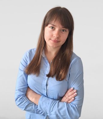 Kobieta w niebieskiej koszuli stoi z założonymi rękoma na białym tle.
