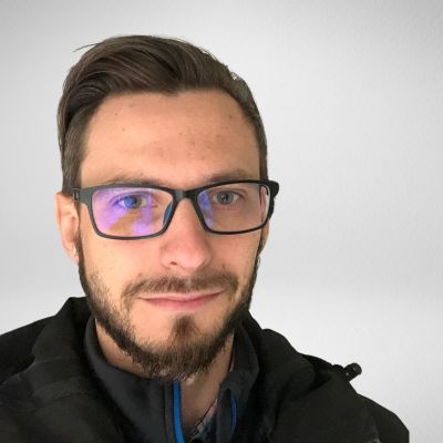 Nie mogę powiedzieć, kto to jest, ale widzę mężczyznę w okularach, z brodą i krótko przyciętymi włosami, patrzącego w kamerę.