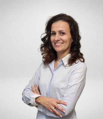 Kobieta w białej koszuli stoi na białym tle, z założonymi rękoma i uśmiechem na twarzy.