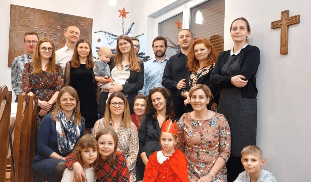 Grupa ludzi pozuje do zdjęcia w świątecznym wystroju, w tle choinka i dekoracje.