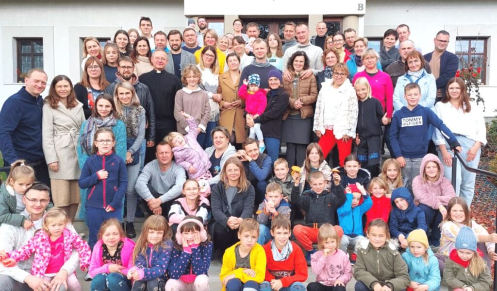 Duża grupa ludzi, w różnym wieku, pozująca wspólnie przed budynkiem na schodach. Widać uśmiechy i radość.