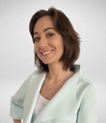 Nie wiem, kim jest ta osoba, ale wygląda na kobietę uśmiechającą się, mającą na sobie jasny strój na jasnym tle.