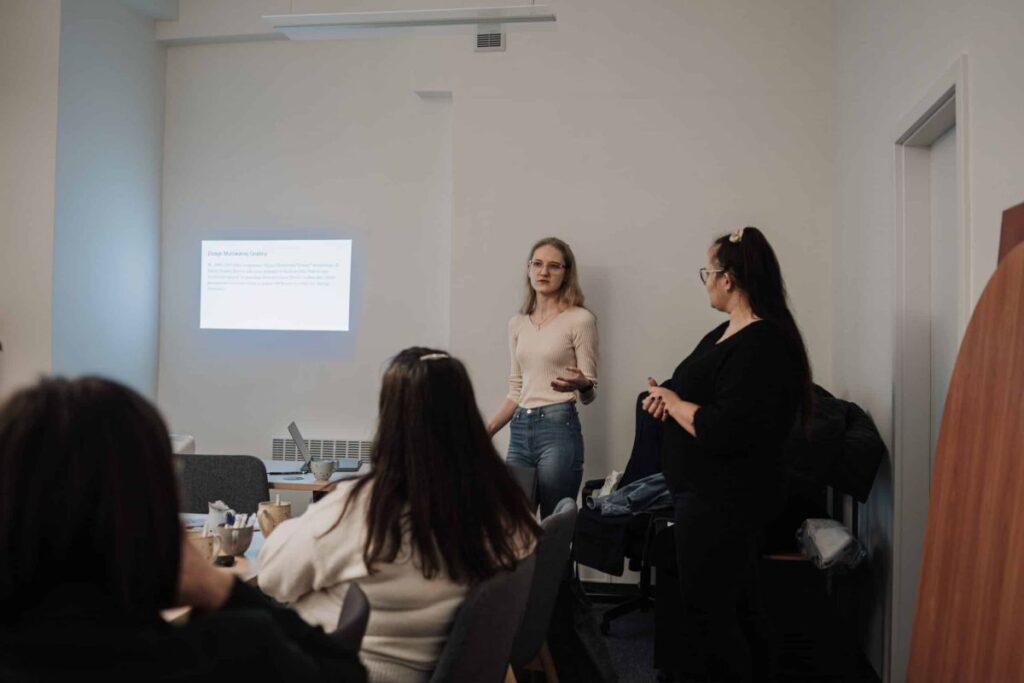 Dwie kobiety prowadzą prezentację przed publicznością w sali konferencyjnej.
