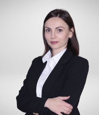 Kobieta w czarnym garniturze z białą koszulą na jasnym tle, z założonymi rękami.